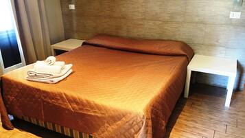 A neatly made bed with a brown bedspread, a folded towel on the bed, and two bedside tables.