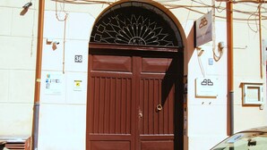 A brown double door with a decorative metal arch above it, set in a building with visible signs and numbered doors. - Casa Aurelia (Palermo)
