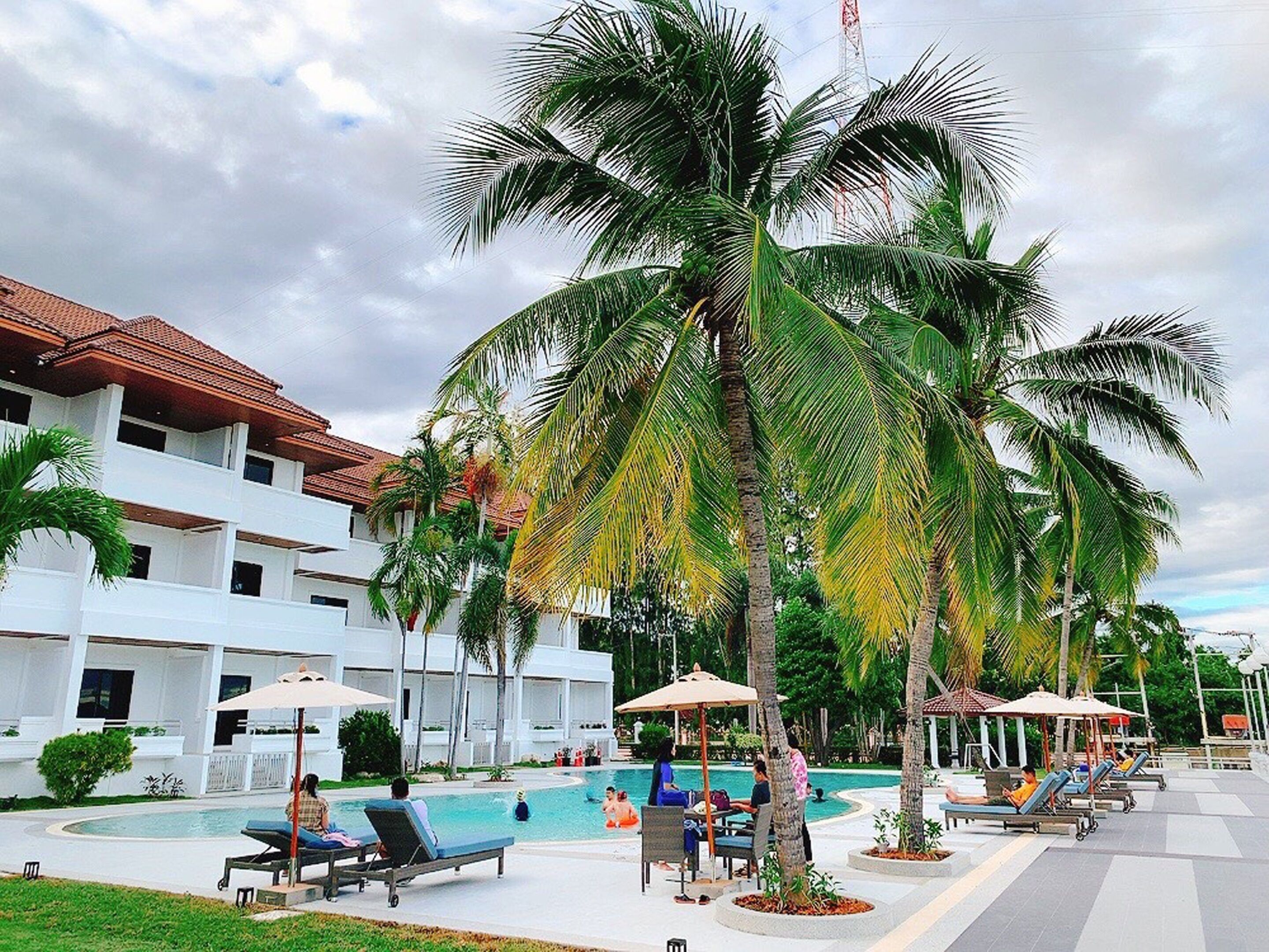 A resort with a swimming pool, palm trees, and a white building with a red roof.