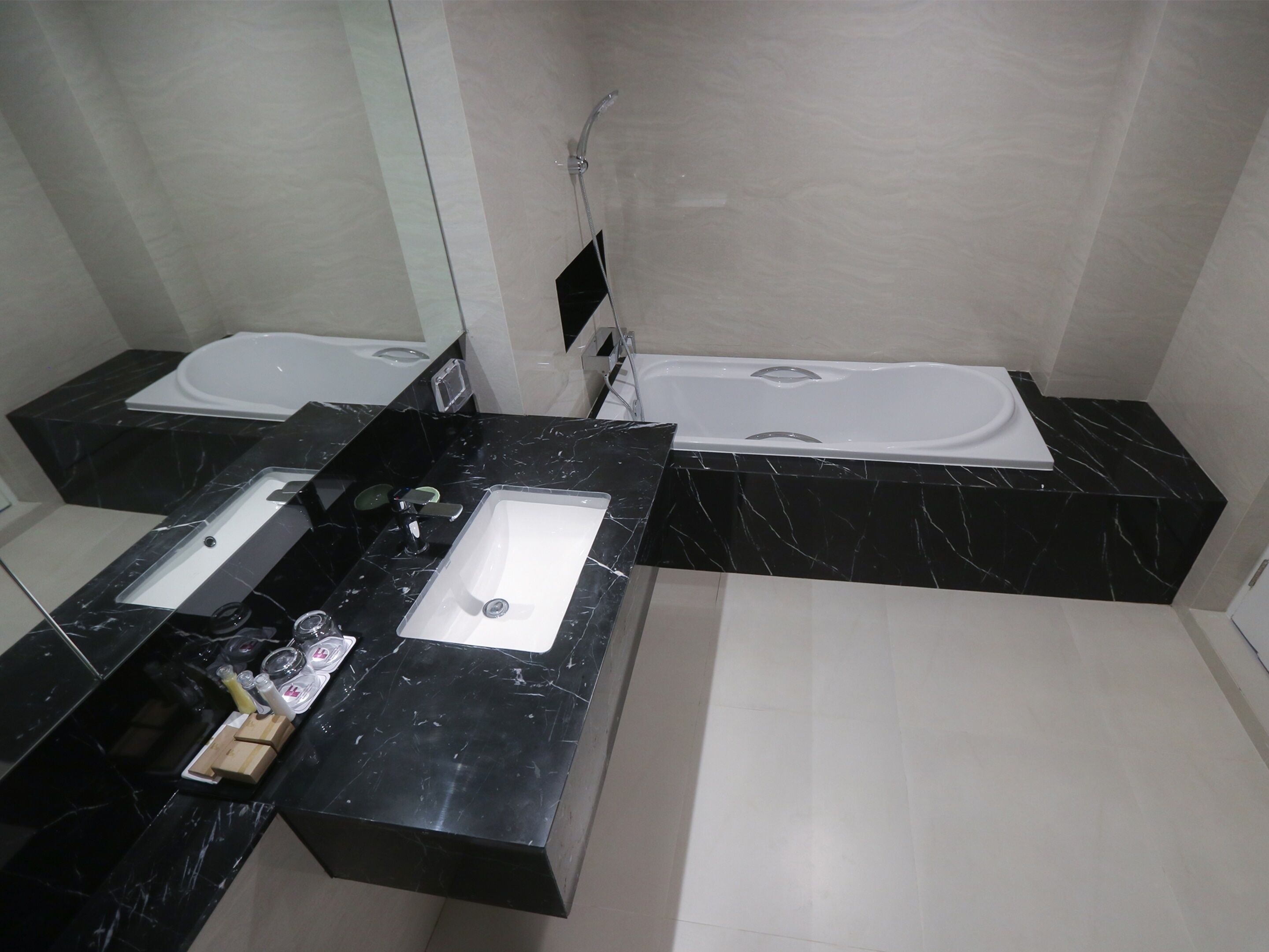 A modern bathroom with a black marble vanity, a large sink, a bathtub, and a shower.
