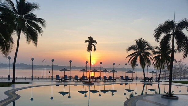 Un espace piscine avec des chaises longues et des parasols, des palmiers et une vue imprenable sur le coucher de soleil.