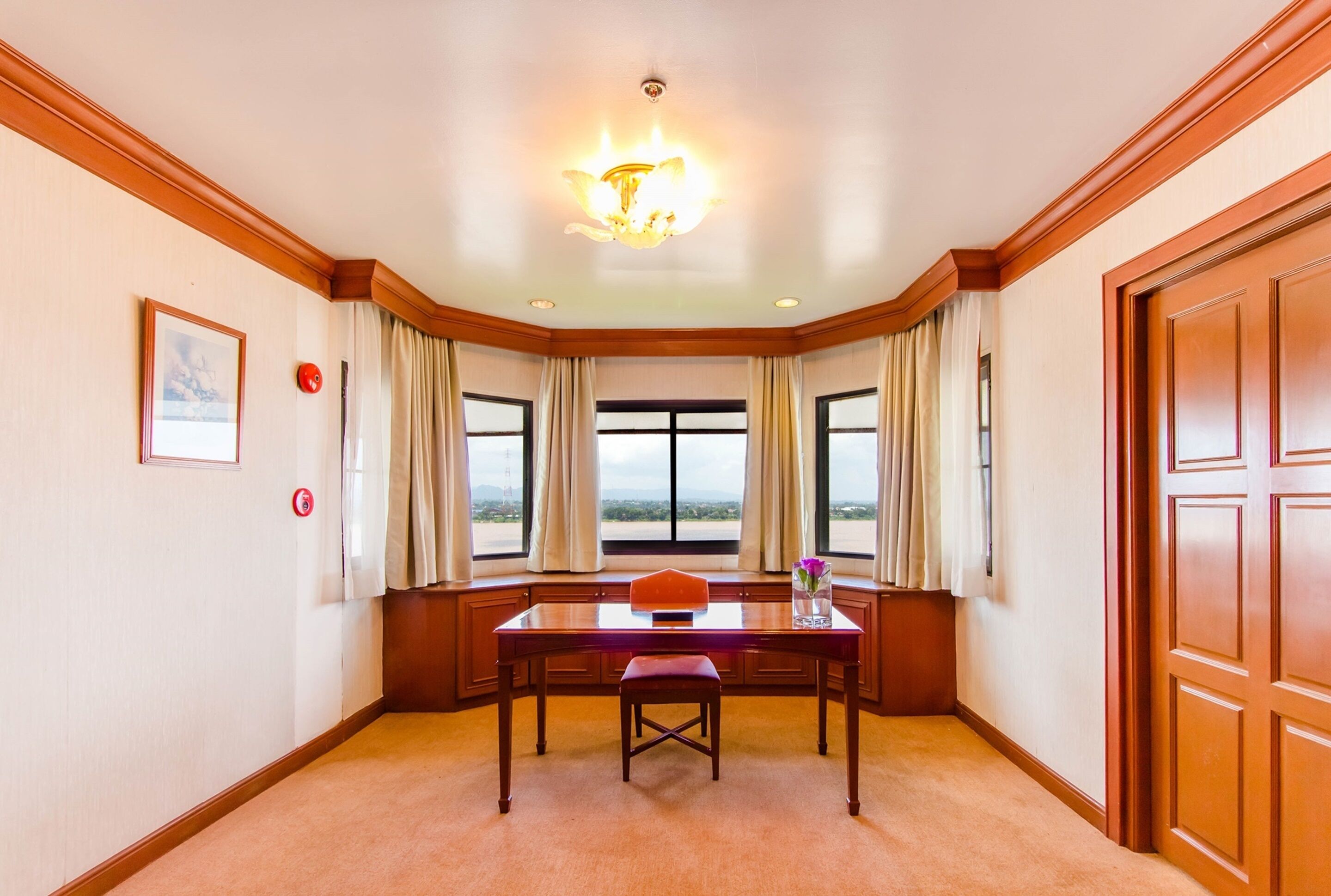 A conference room with a wooden table, a chair, a chandelier, and large windows with curtains.
