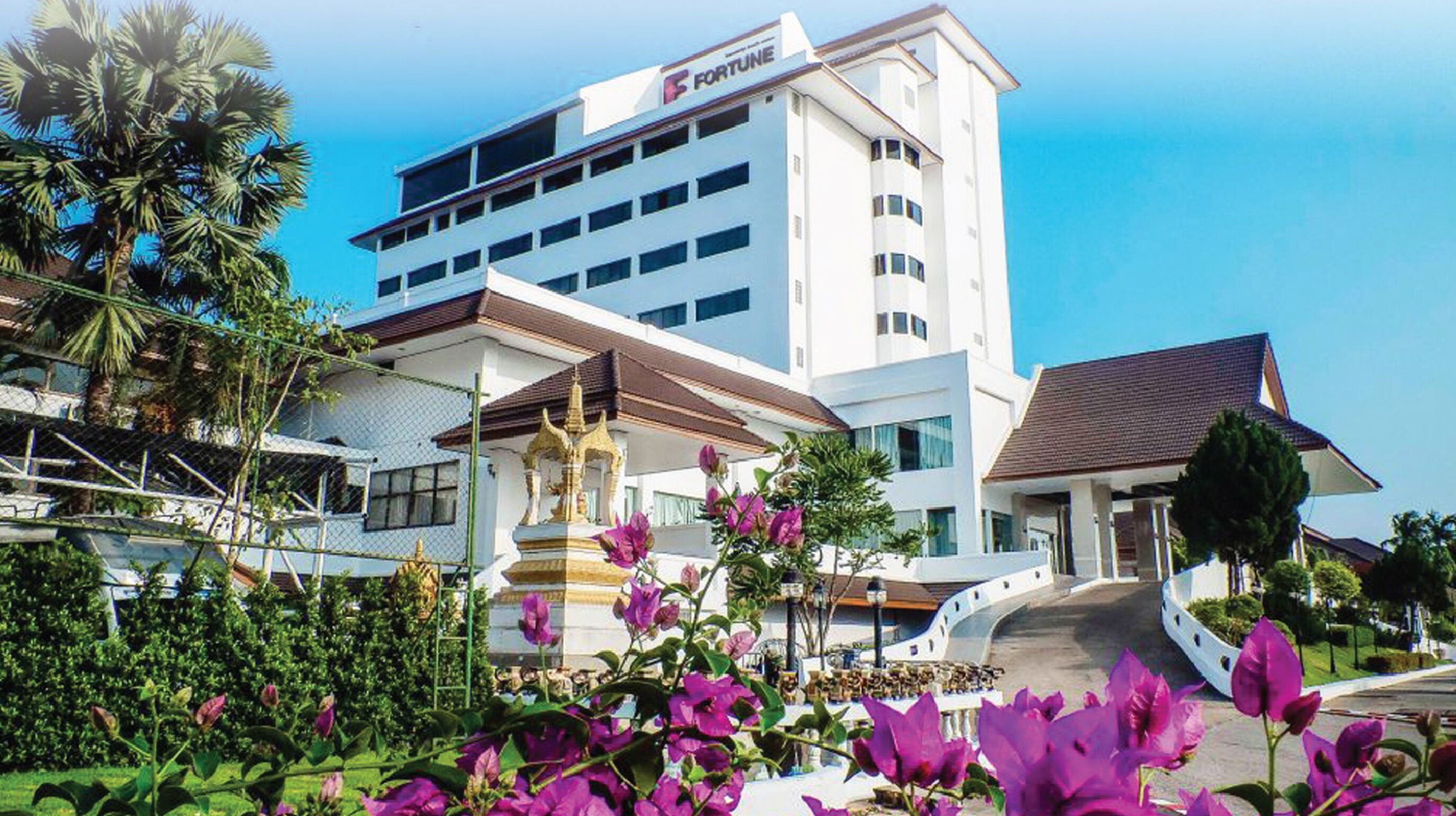 A modern hotel with a prominent 'FORTUNE' sign, a central courtyard with a golden statue, and lush greenery.