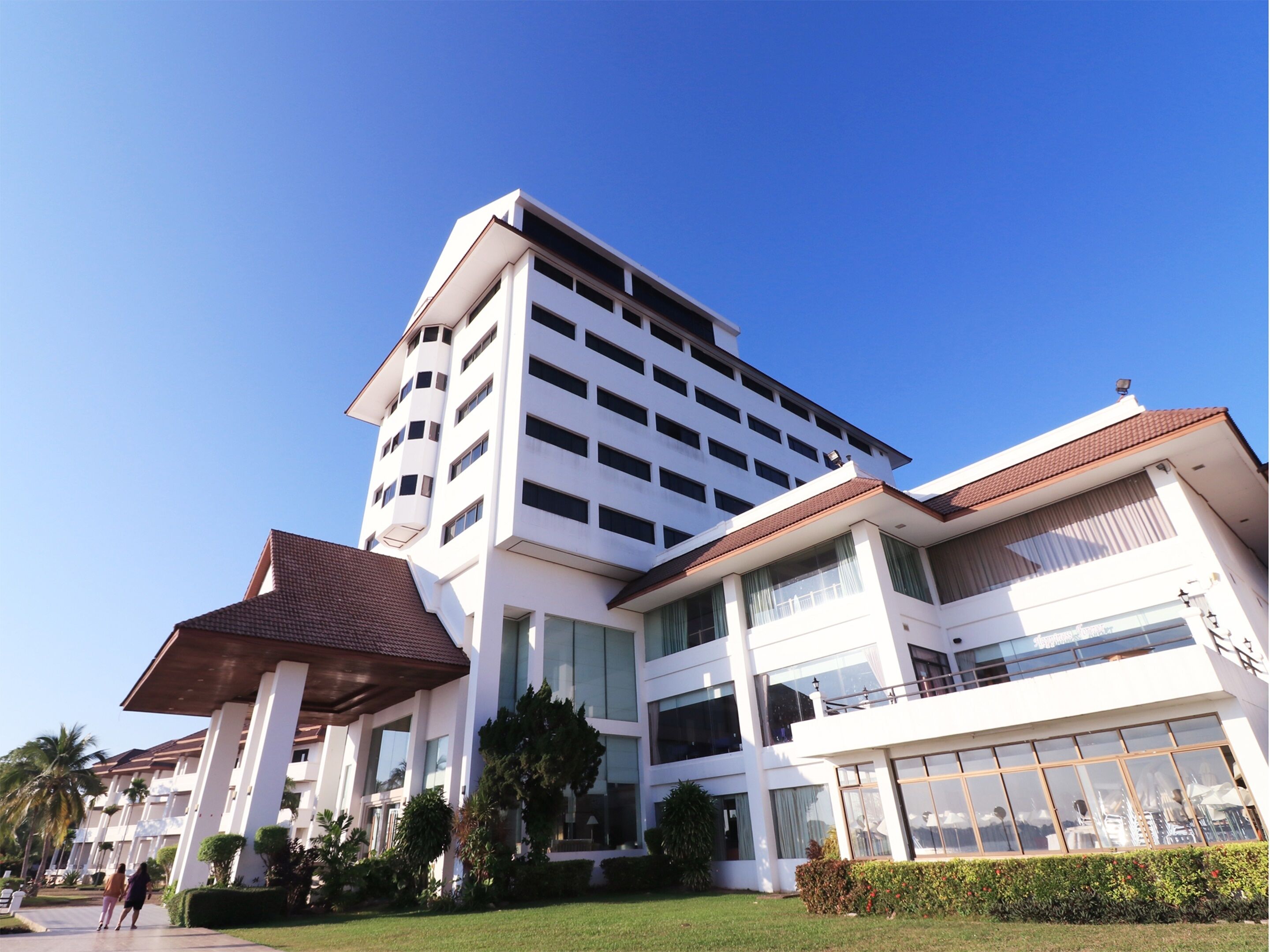 Un hotel de varios pisos con un diseño arquitectónico moderno, que destaca por una entrada prominente con zona cubierta y un césped bien cuidado.