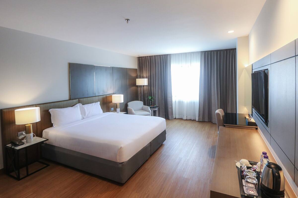 Una habitación de hotel moderna con una cama grande, mesitas de noche con lámparas, un televisor de pantalla plana y una cafetera.