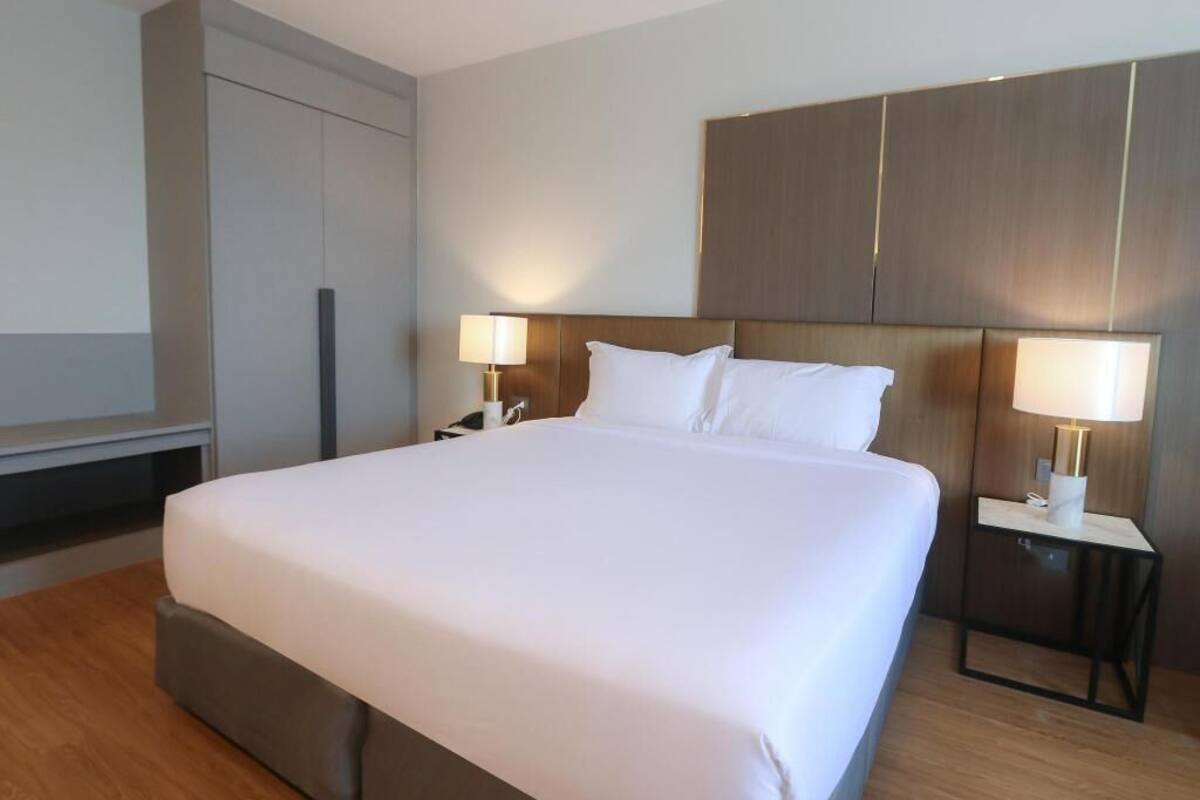 Una habitación de hotel con una cama grande, lámparas de noche, un televisor y un armario.