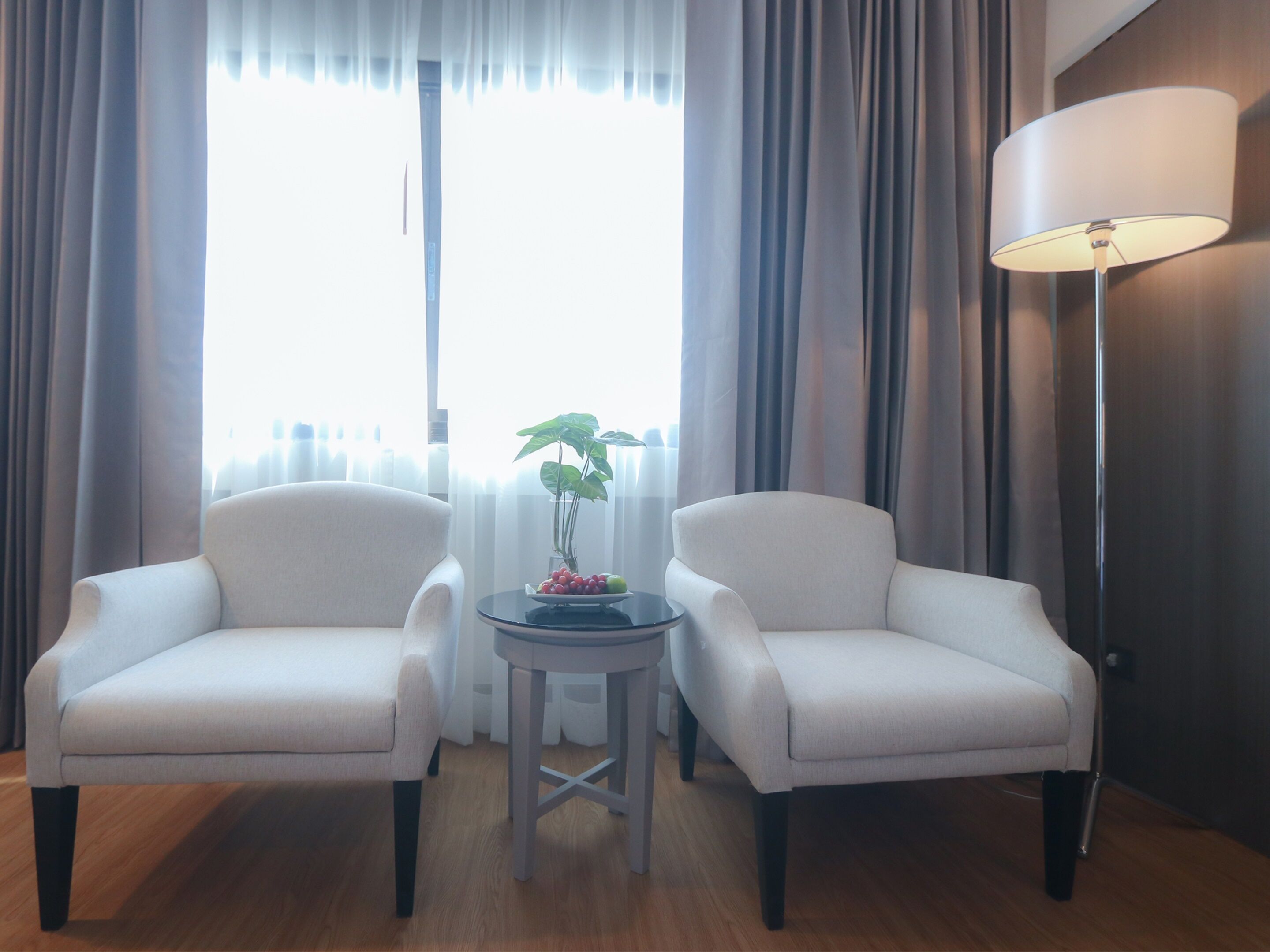 A room with two white armchairs, a small round table with a plant, and a floor lamp.