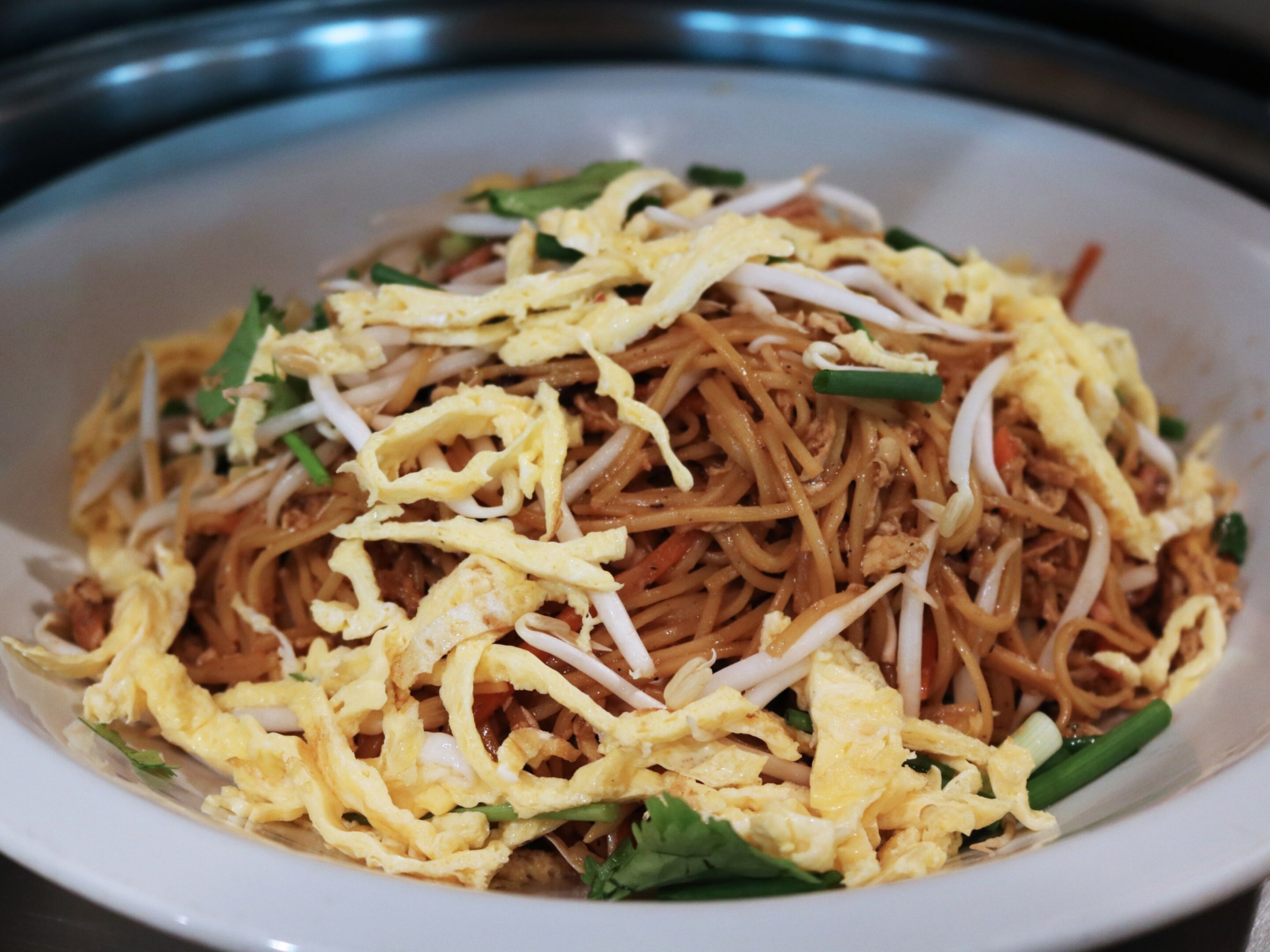Un tazón de fideos cubierto con huevos revueltos y brotes de soja.
