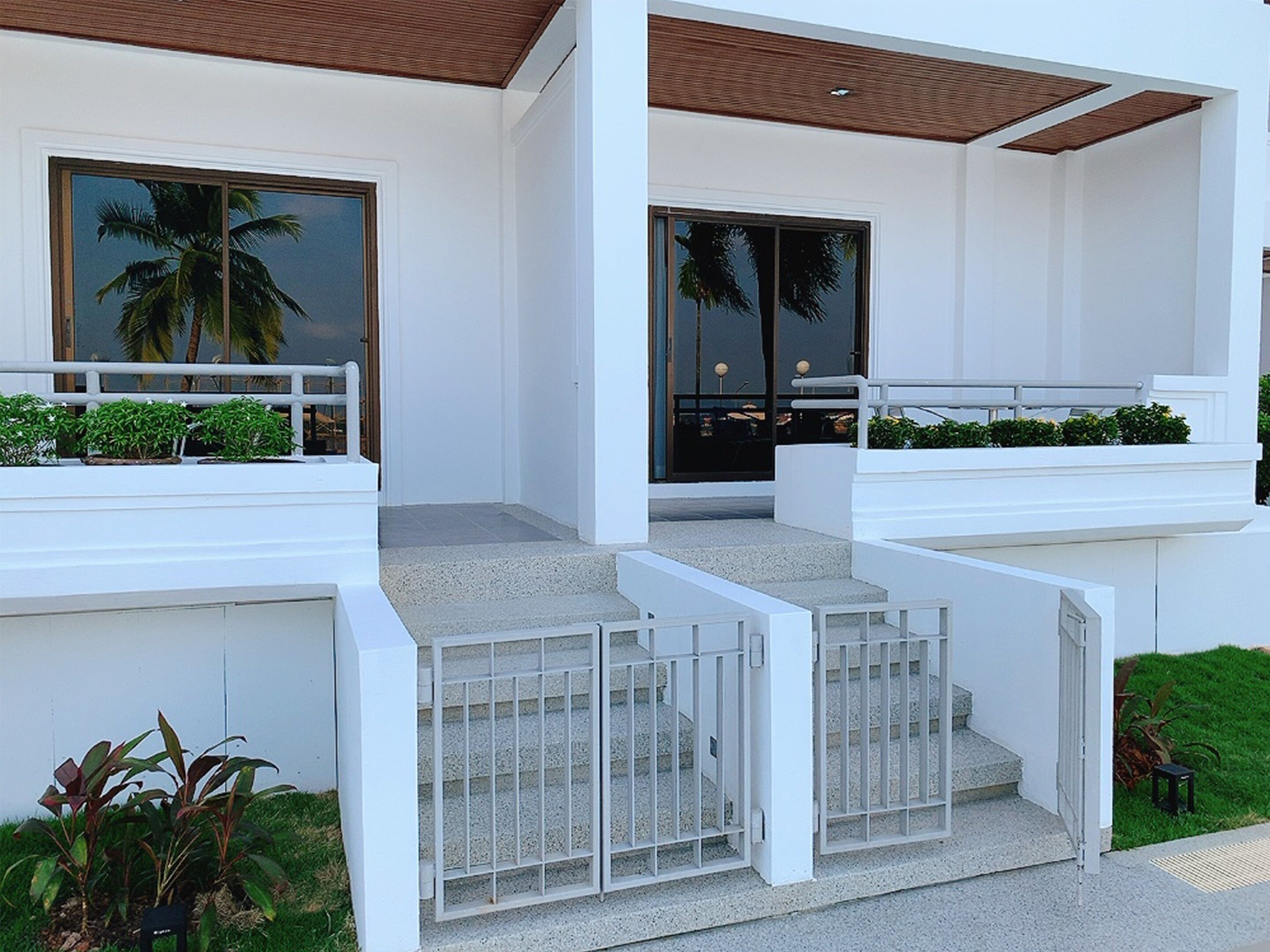 A modern building with a white exterior, a wooden ceiling, and a set of concrete steps leading to a glass door.