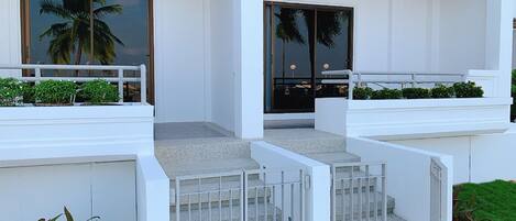A modern building with a white exterior, a wooden ceiling, and a set of concrete steps leading to a glass door.