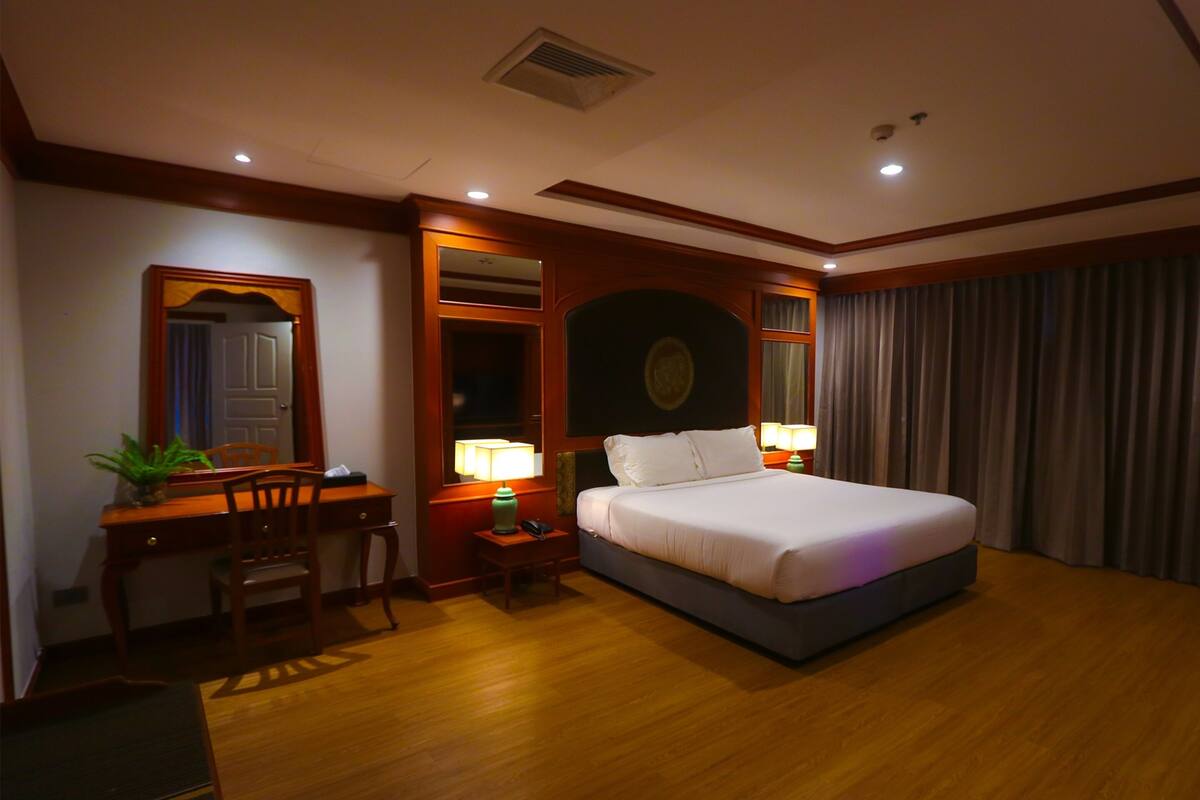 Habitación de hotel con una cama grande, un escritorio con silla, una mesita de noche con lámpara y una planta en maceta.