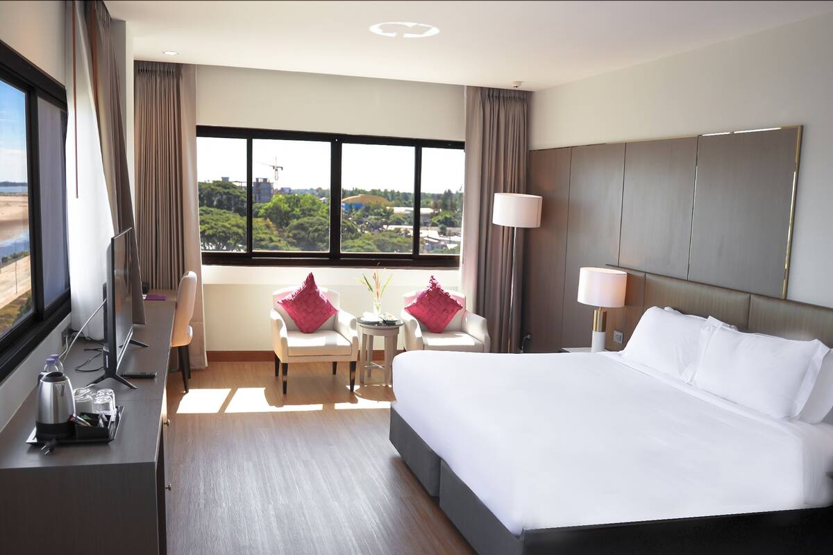 Una habitación de hotel moderna con una cama grande, un escritorio, una silla y vistas a la ciudad.