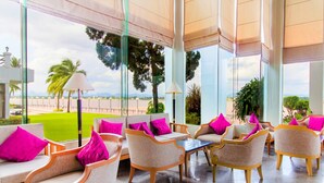 Un espace de détente moderne, doté de sièges confortables et de grandes fenêtres offrant une vue sur un jardin paysager et des palmiers.