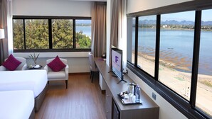 Une chambre d’hôtel équipée d’un lit, d’un bureau, d’une chaise et d’une grande fenêtre donnant sur un lac et des montagnes.