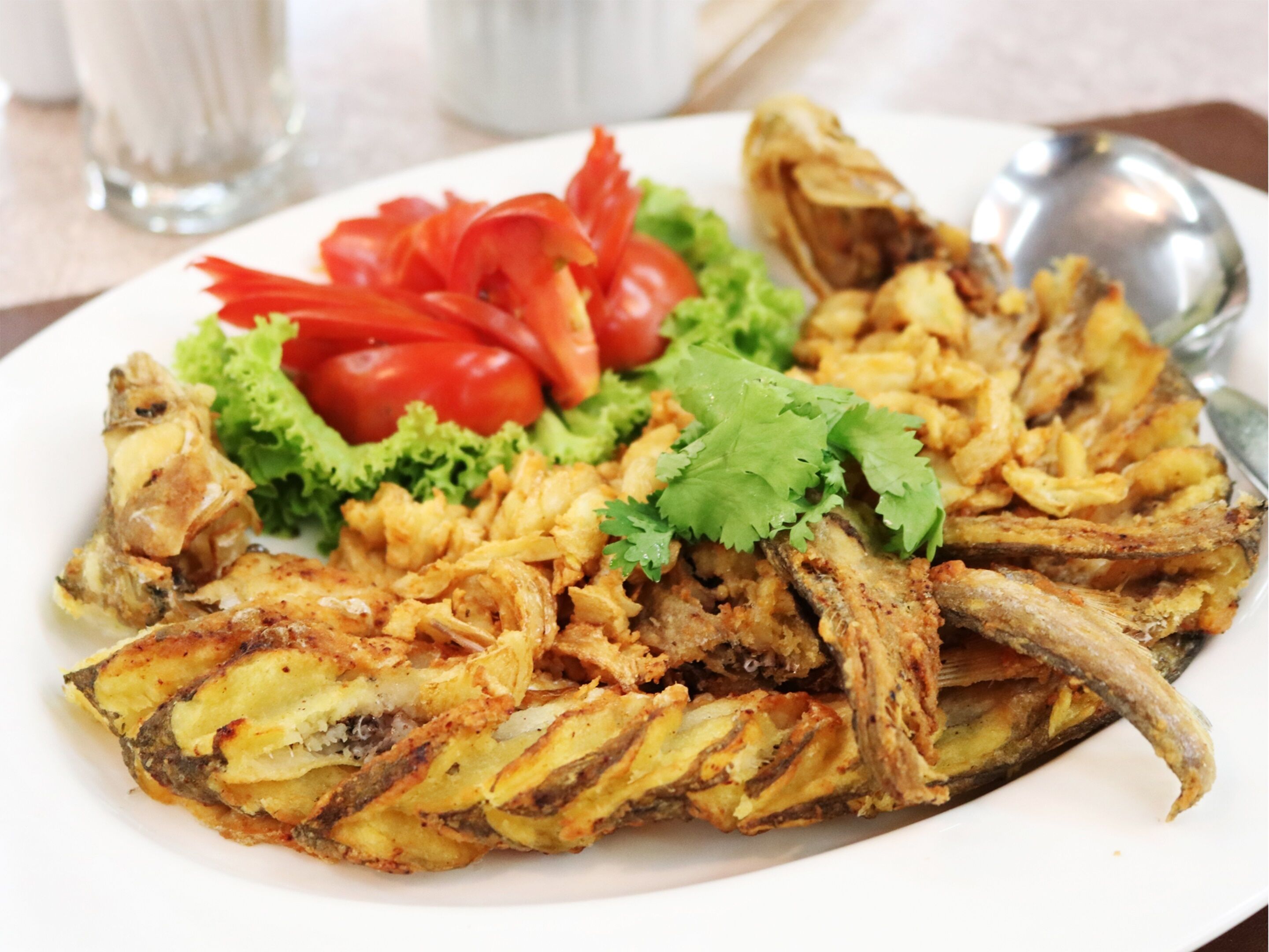 Un plato de pescado frito acompañado de verduras, pimientos rojos y lechuga.