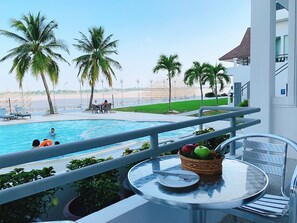 Blick auf einen Pool mit Essbereich, Palmen und einem Strand im Hintergrund.