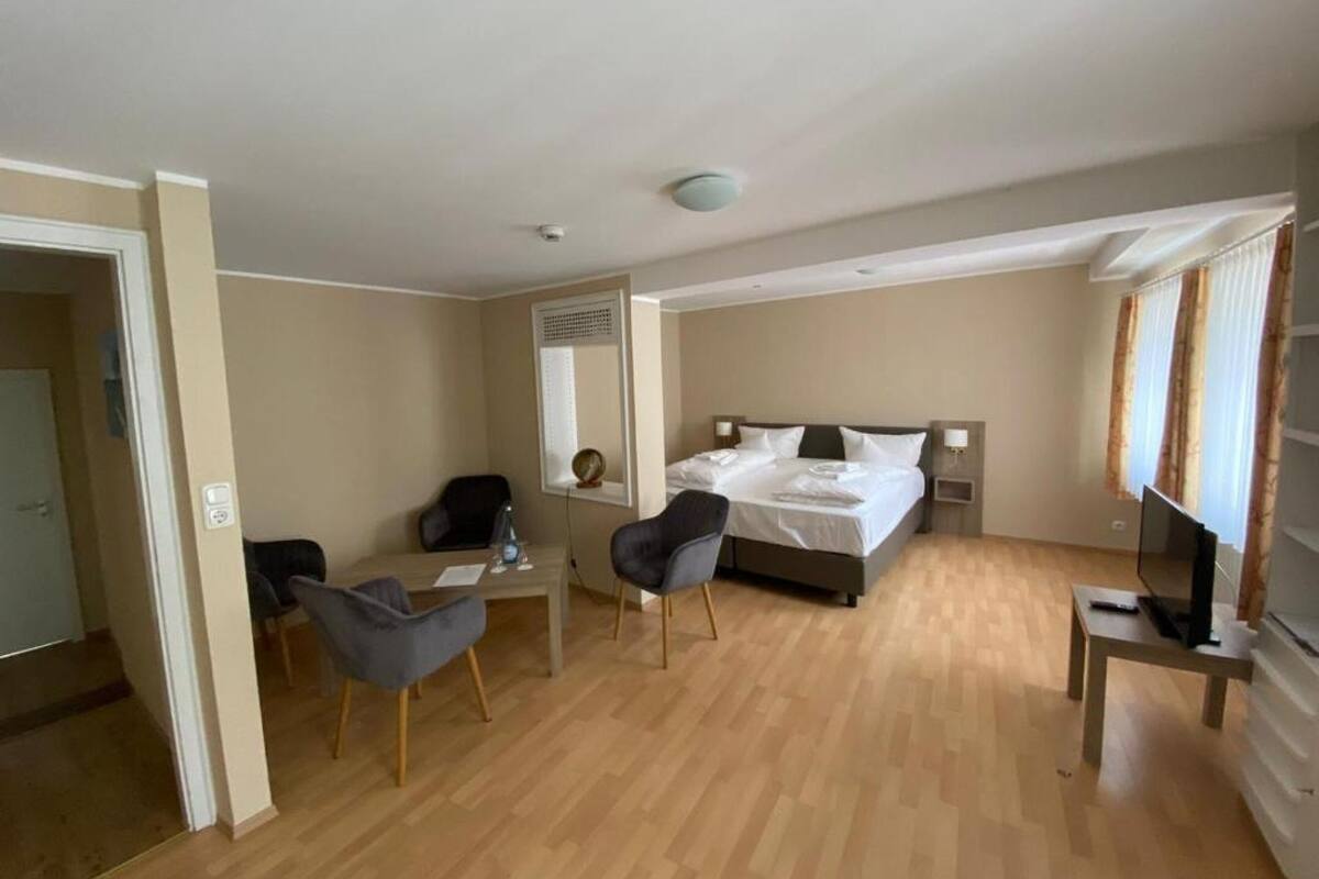 Ein Hotelzimmer mit Bett, Schreibtisch, zwei Stühlen, einem Fernseher und einem Fenster mit Vorhängen.