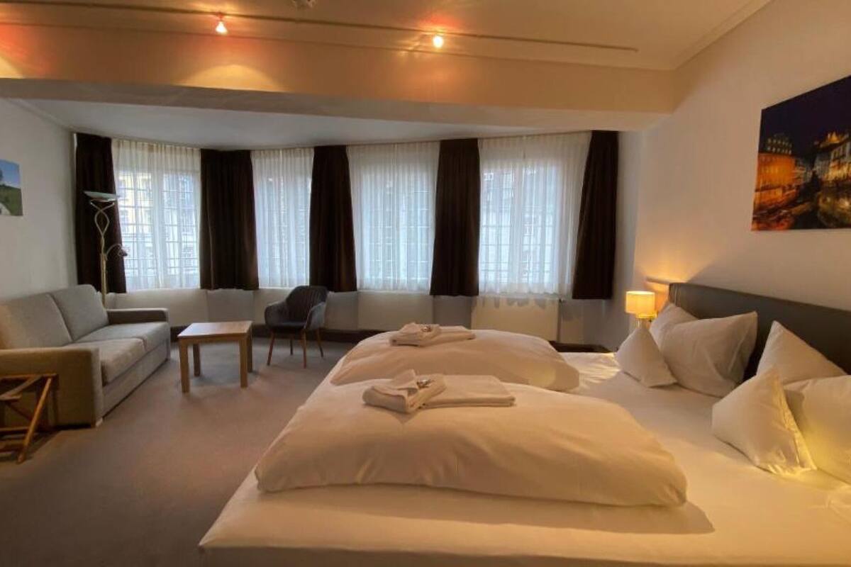 Ein Hotelzimmer mit einem großen Bett, einer Couch, einem Sessel, einem kleinen Tisch und einem Fenster mit Vorhängen.