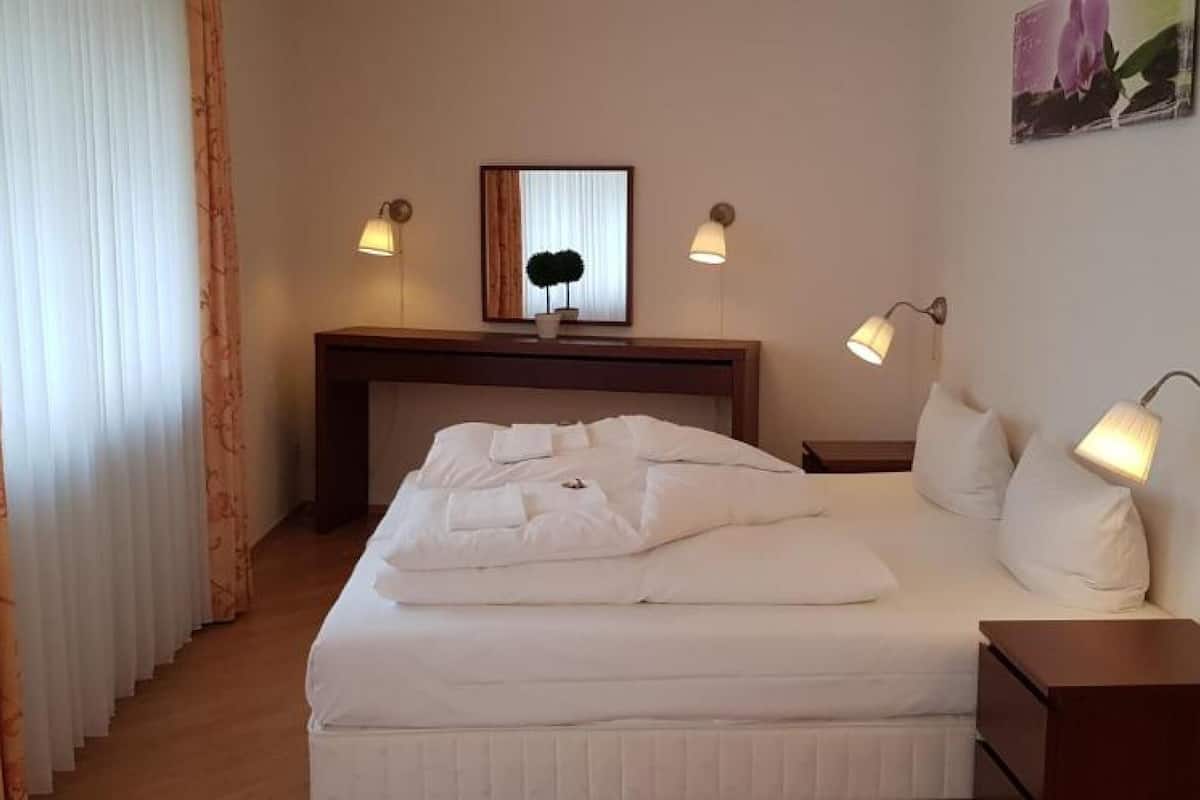 Ein Hotelzimmer mit einem ordentlich bezogenen Bett, einem Schreibtisch mit Stuhl, einem kleinen Tisch und zwei Wandleuchten.
