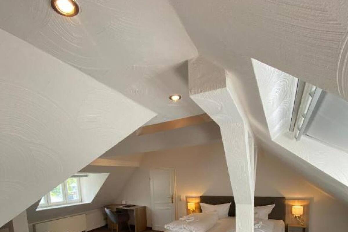 Ein modernes Schlafzimmer mit Schräge, einem Bett, Nachttischen, einem Schreibtisch und einem Sessel.