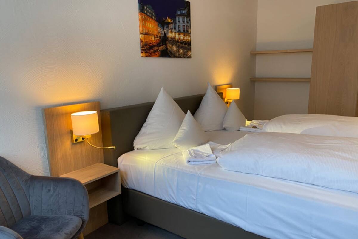 Ein Hotelzimmer mit einem Bett, zwei Nachttischen mit Lampen, einem Sessel und einem Bild an der Wand.