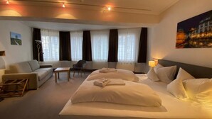A hotel room with a large bed, a sofa, a chair, a small table, and a window with curtains. - Hotel Horchem (Monschau)