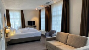A hotel room with a bed, a sofa, a TV, and curtains. - Hotel Horchem (Monschau)