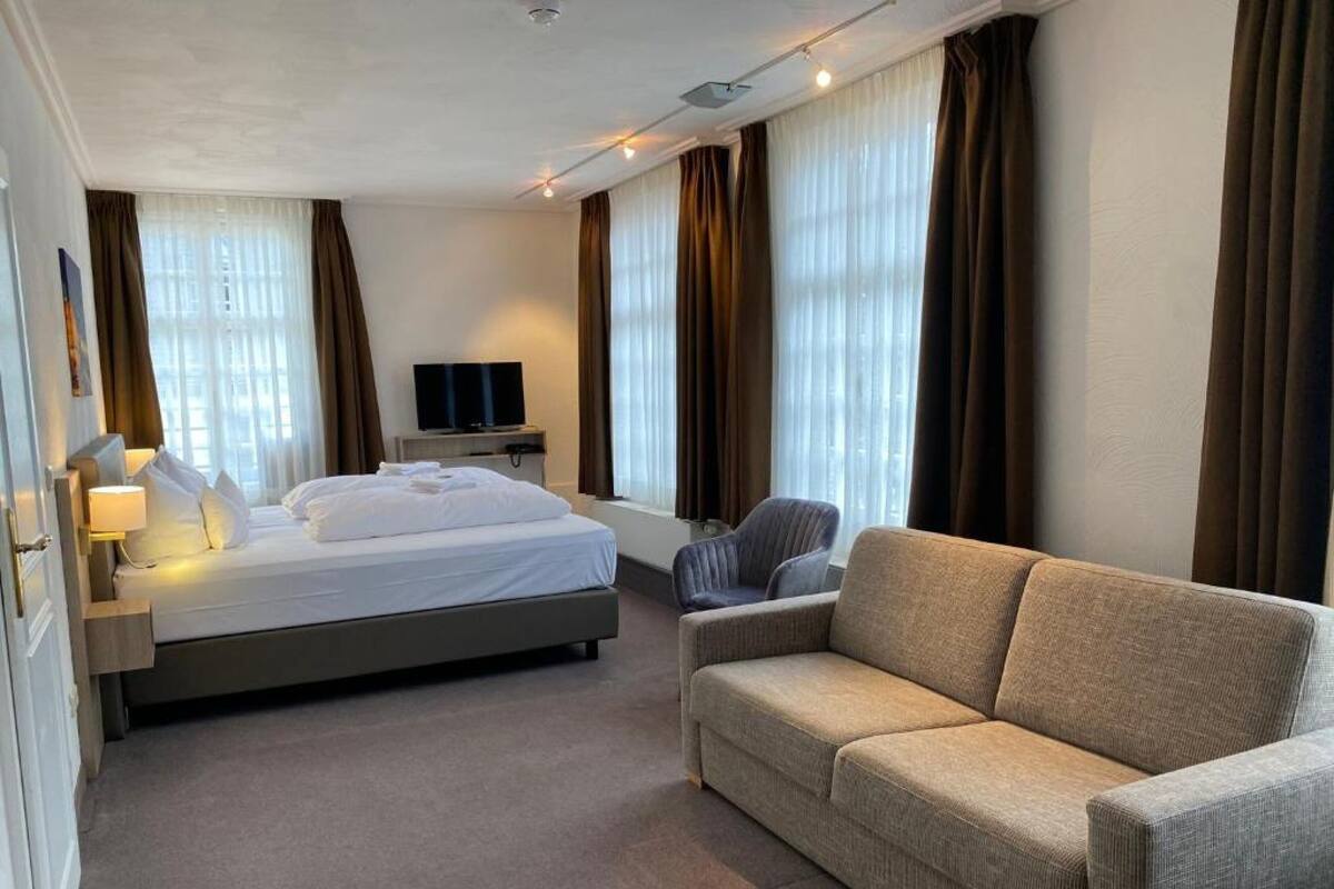 Ein Hotelzimmer mit Bett, einer Couch, einem Fernseher und Vorhängen.