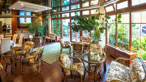 Een ruime lobby met rieten meubels, grote ramen en kamerplanten.