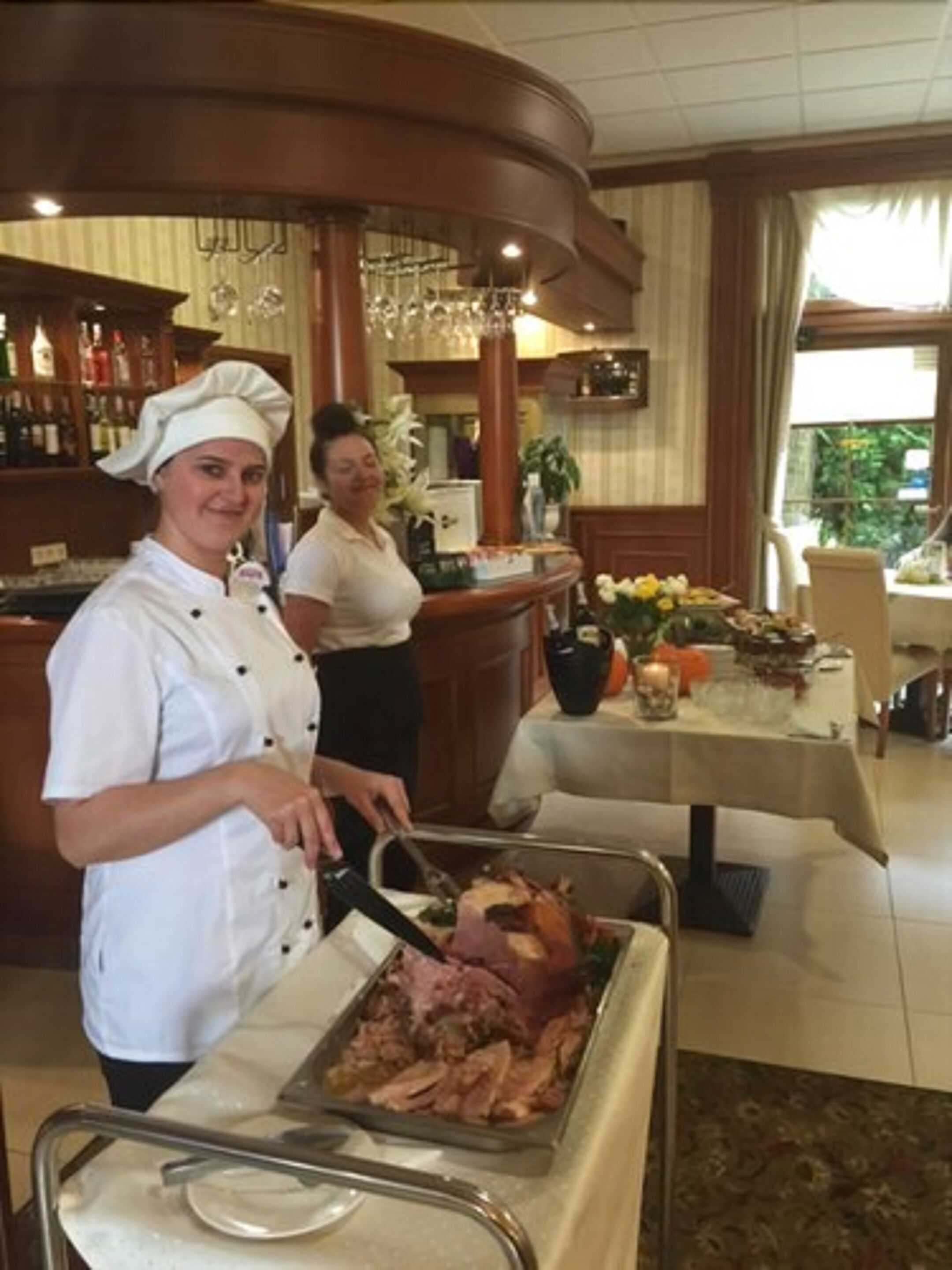 A buffet setup with a chef preparing food, a bar area in the background, and a dining table with a floral centerpiece.