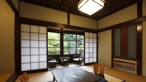 A traditional Japanese room with tatami flooring, a low table, and a view of greenery outside. - Hazuki (Shinshiro)