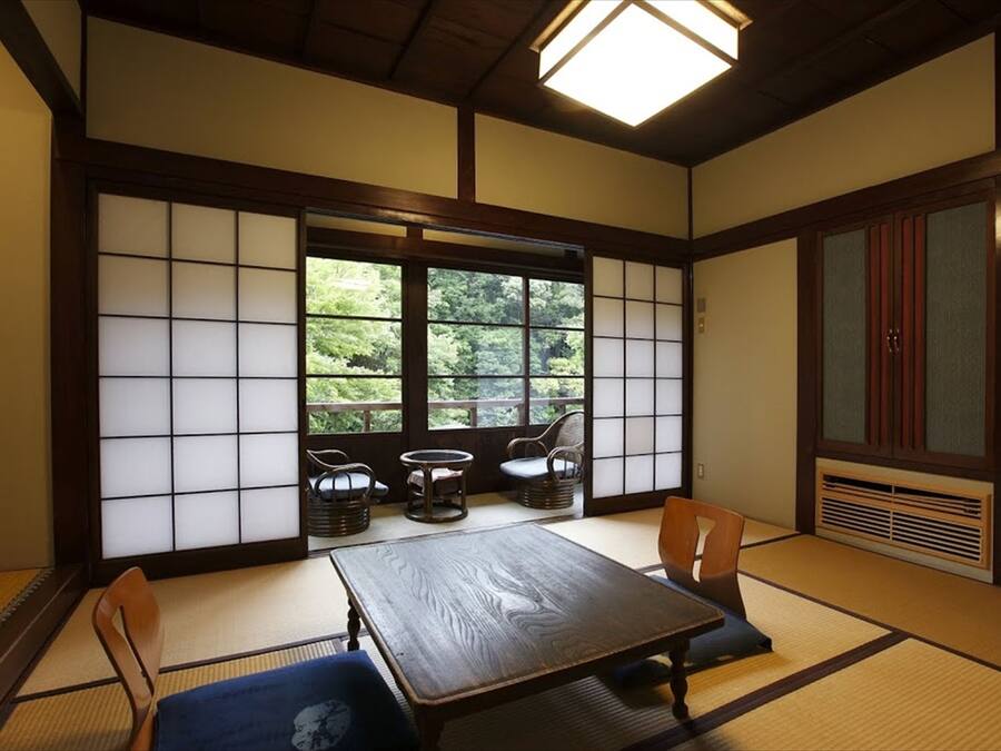 A traditional Japanese room with tatami flooring, a low table, and a view of greenery outside.