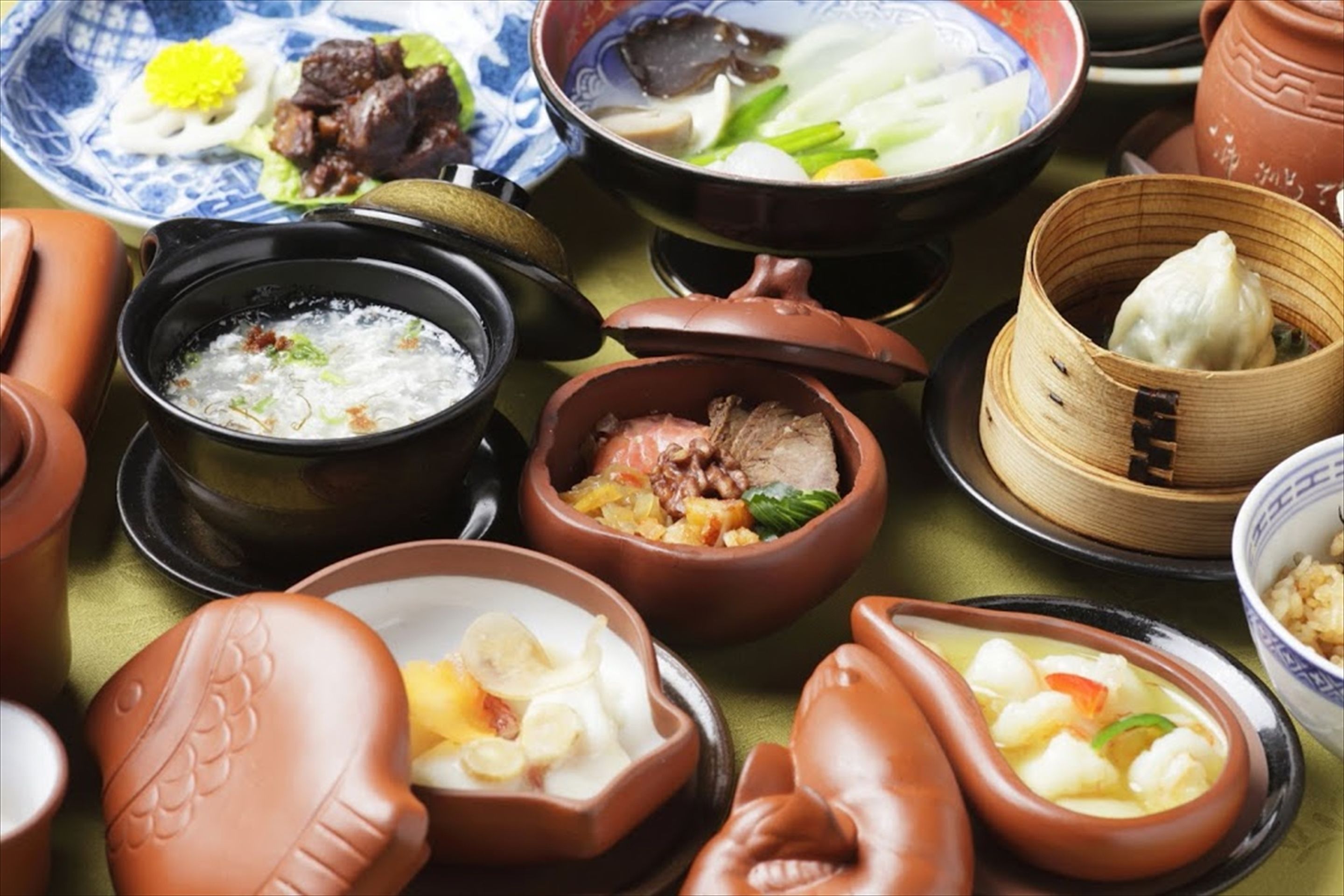 A variety of traditional dishes in clay pots and a bamboo steamer, suggesting a cultural dining experience.