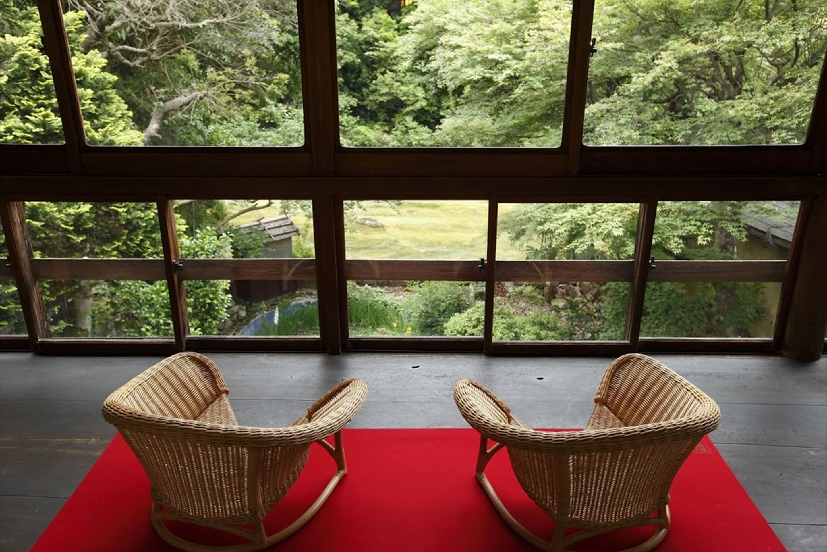 A room with two wicker rocking chairs facing a large window overlooking a lush garden.