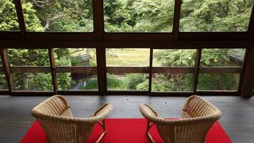 A room with two wicker rocking chairs facing a large window overlooking a lush garden.