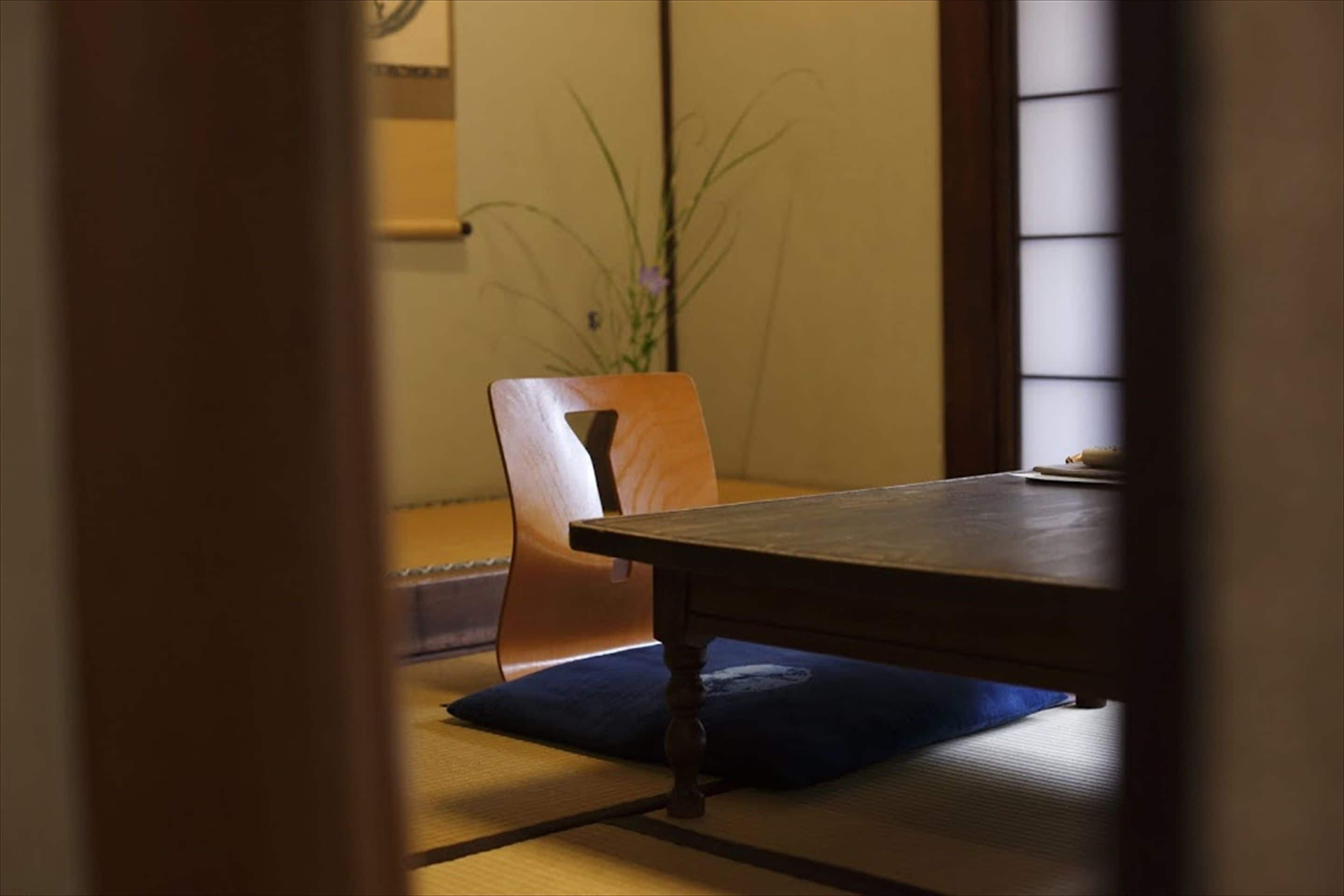A traditional Japanese room with tatami flooring, a low wooden table, and a chair with a blue cushion.