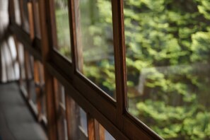 A view through a window with a wooden frame, focusing on the window's edge and a blurred green outdoor scene.