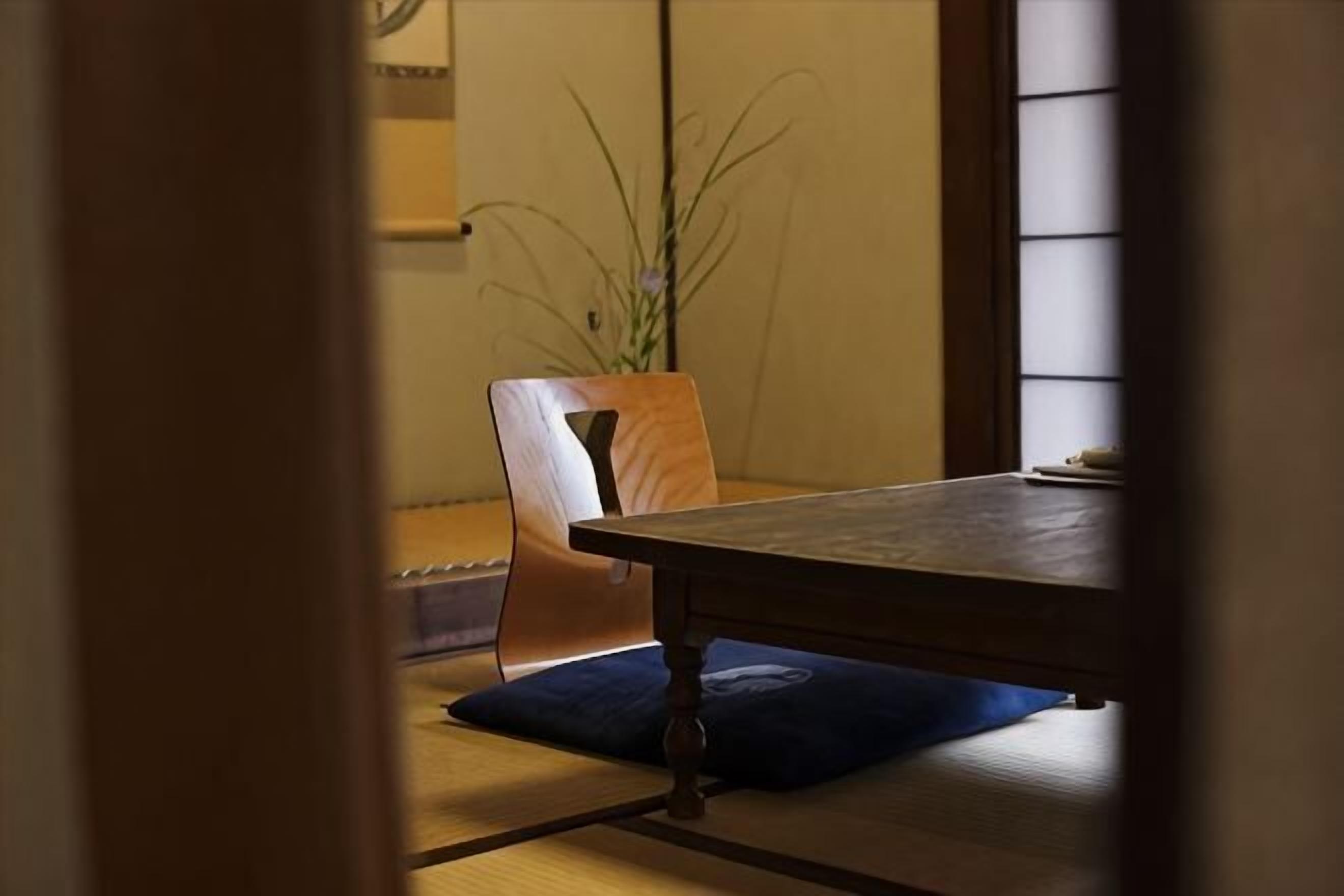 Una habitación tradicional japonesa con suelo de tatami, una mesita baja y una silla de madera.