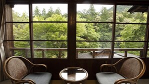 A room with two wicker chairs and a small glass table, large windows with a view of a forested area. - Hazuki (Shinshiro)