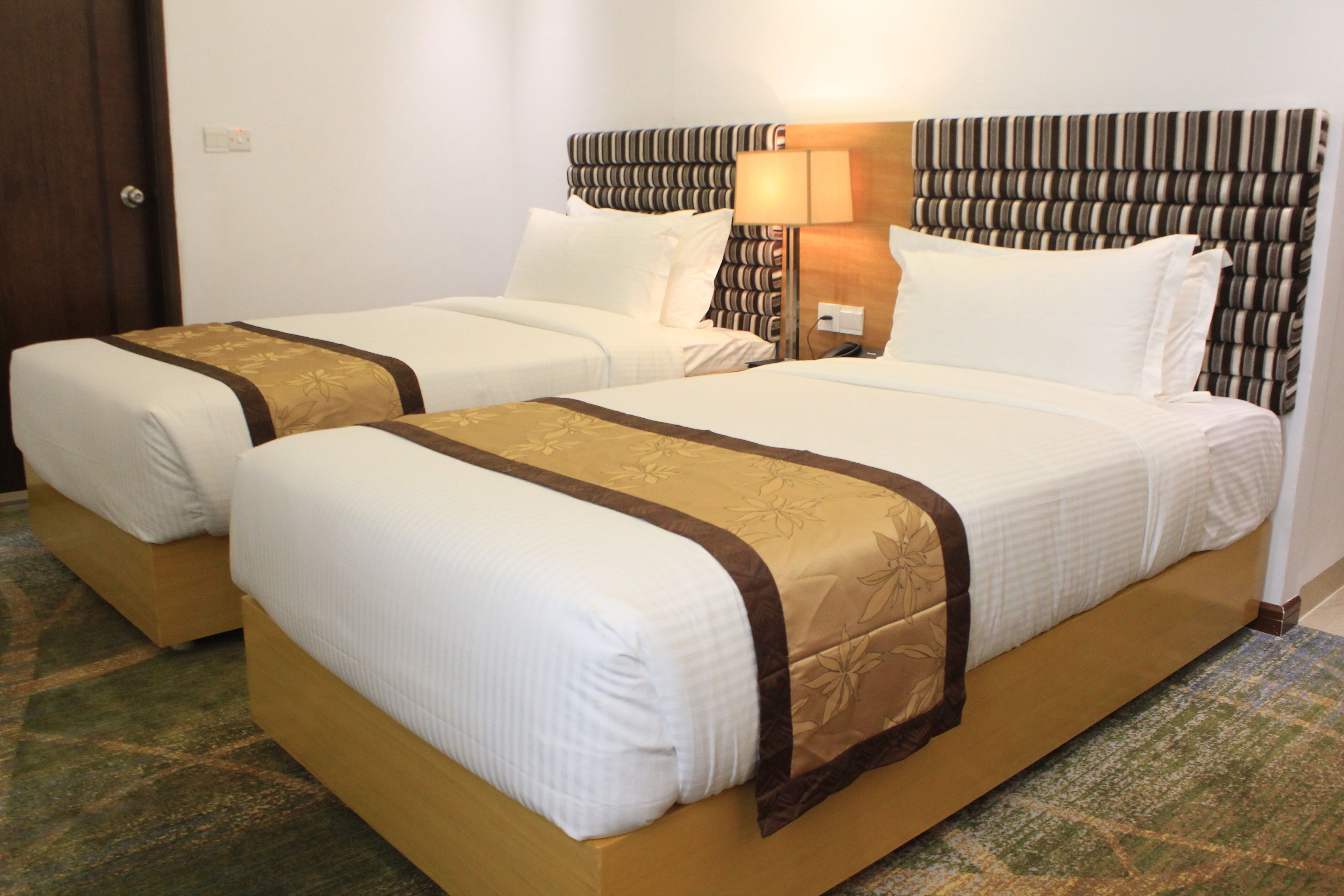 A hotel room with two single beds, a wooden headboard, a nightstand, and a patterned carpet.