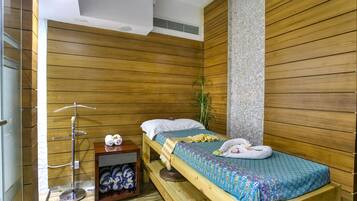 A wooden room with a bed, a small table, and a shelf with towels.
