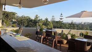An outdoor patio with wicker furniture, a table, and hanging light fixtures. - Arcadia Suites (Kampala)