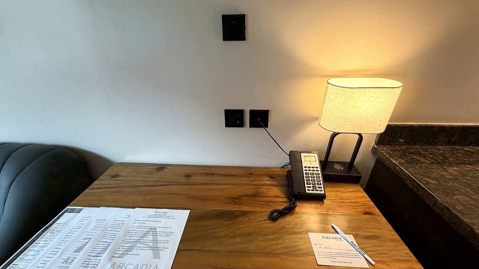 A wooden nightstand with a lamp, a telephone, and papers.
