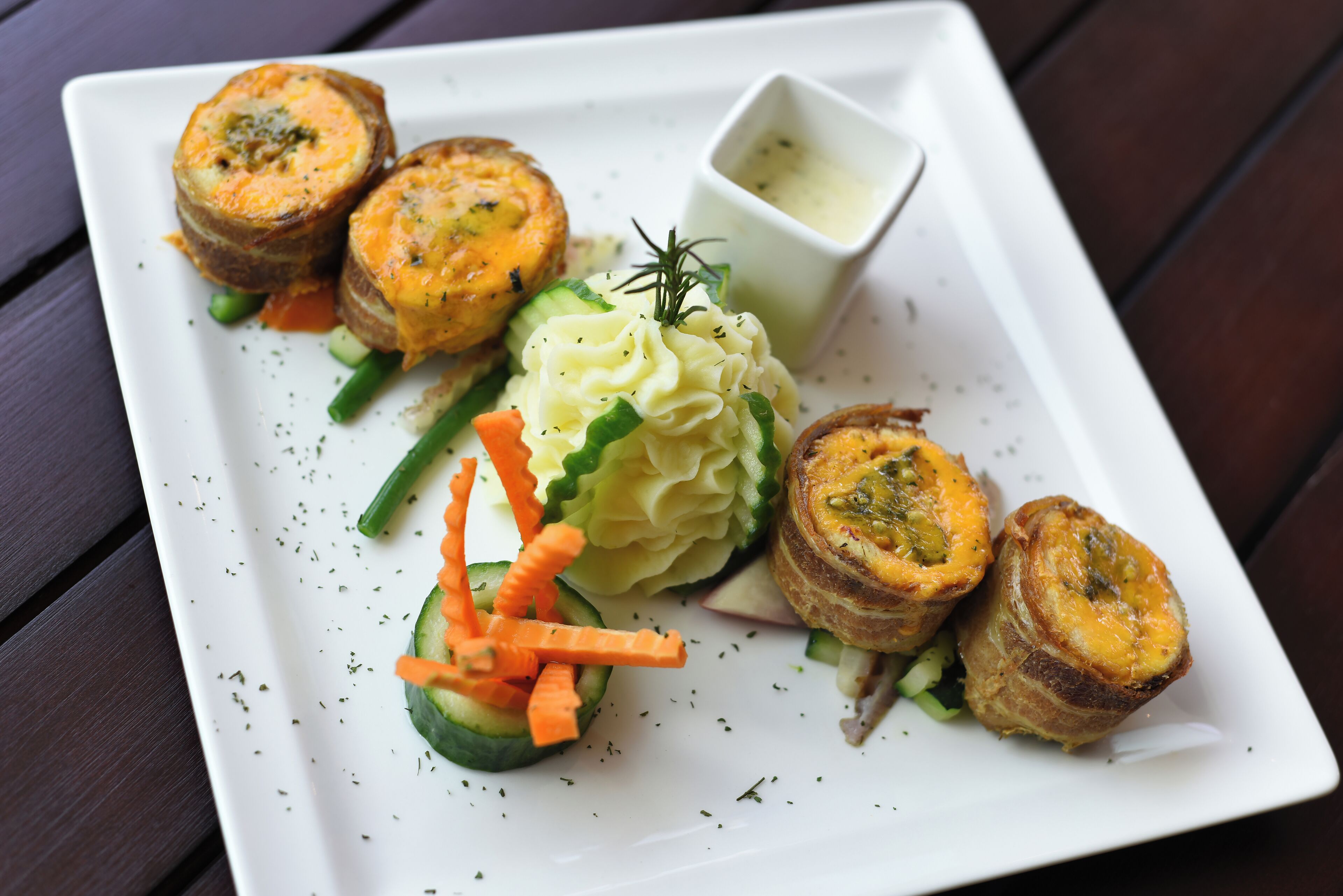 A white plate with food items including rolled vegetables, mashed potatoes, and a small bowl of sauce.