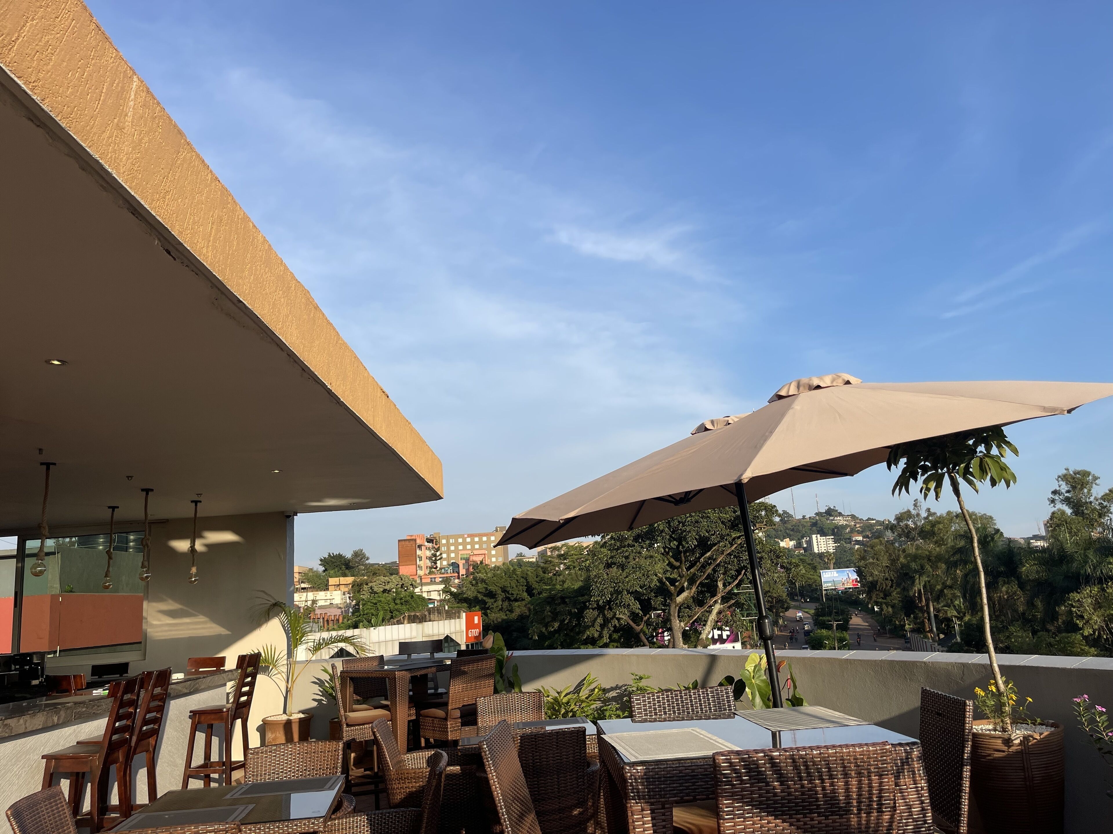 An outdoor seating area with wicker furniture and umbrellas, overlooking a cityscape.