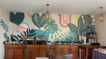Un restaurante con un vibrante mural tropical, armarios de madera y una zona de bar con una máquina de café.