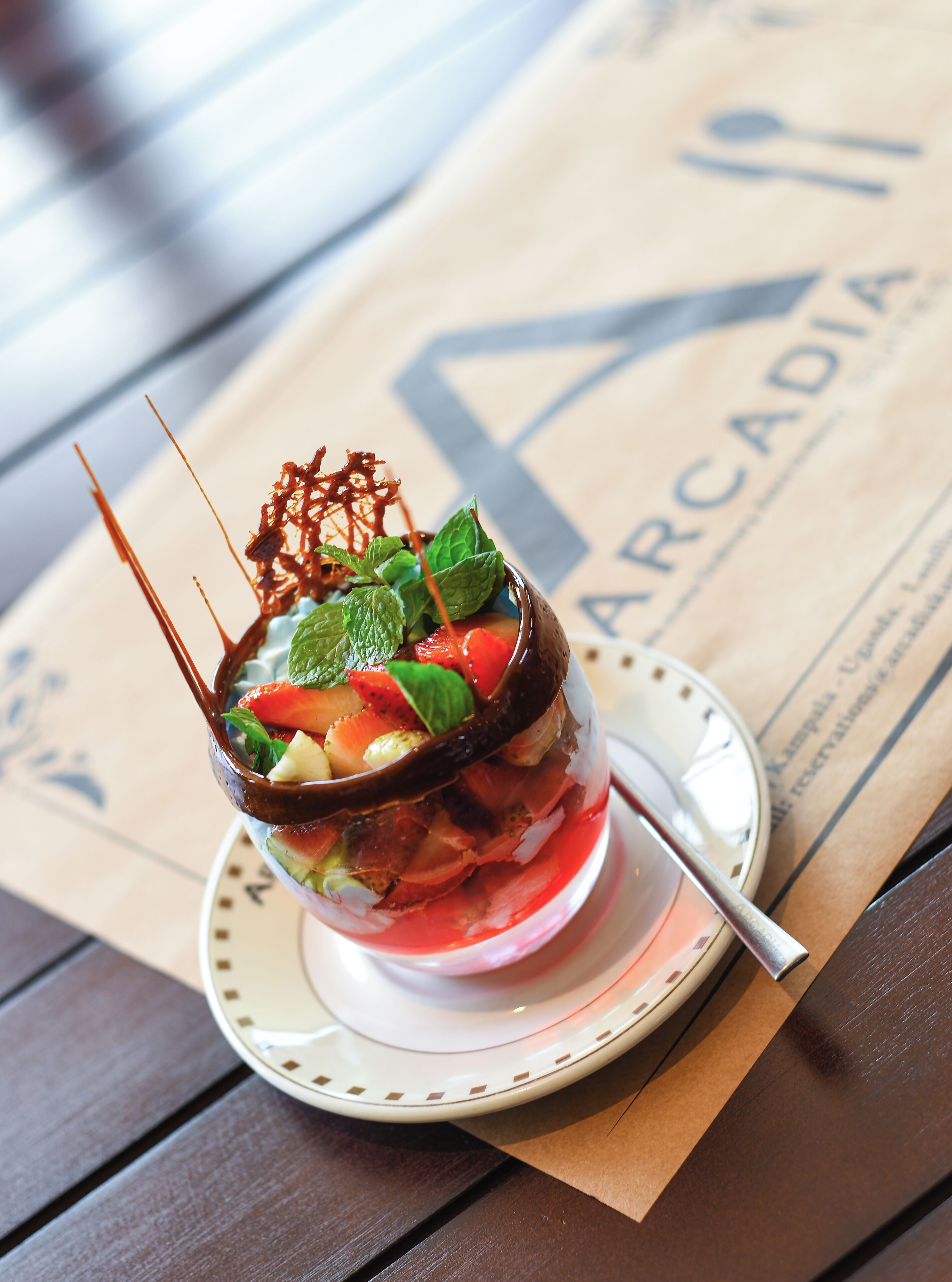 A dessert in a glass bowl on a saucer, placed on a wooden table with a napkin underneath.