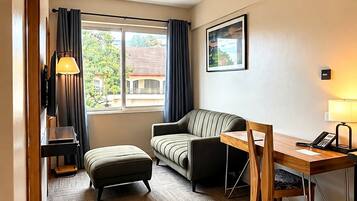 Habitación de hotel con sofá, una mesa de madera, lámpara, escritorio, teléfono y ventana con cortinas.
