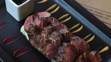 A steak with a side of sauce on a black plate, placed on a table with a paper featuring the word "ARCADIA" in the background.