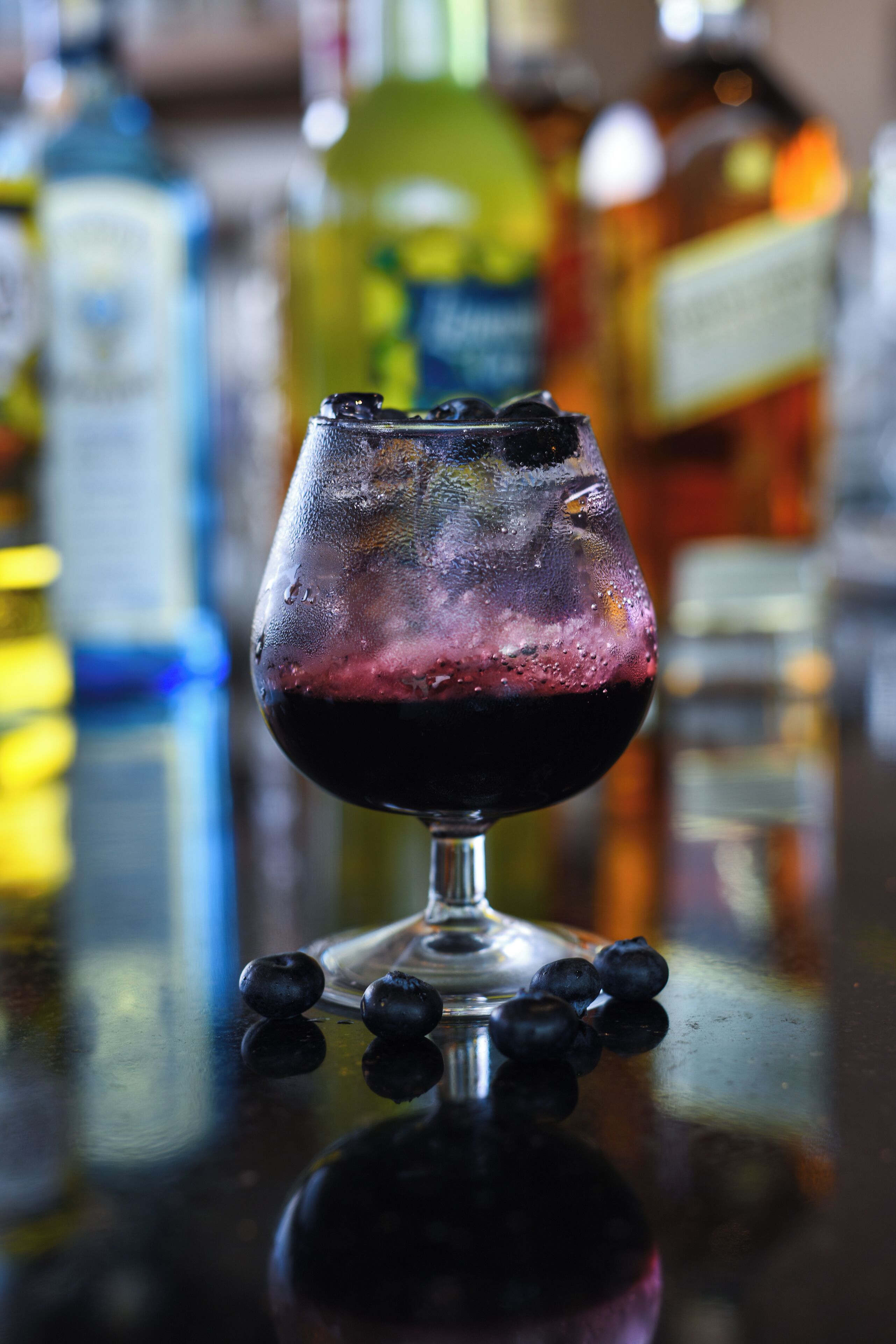 Ein Glas Rotwein mit Eiswürfeln und Blaubeeren auf einer spiegelnden Oberfläche.